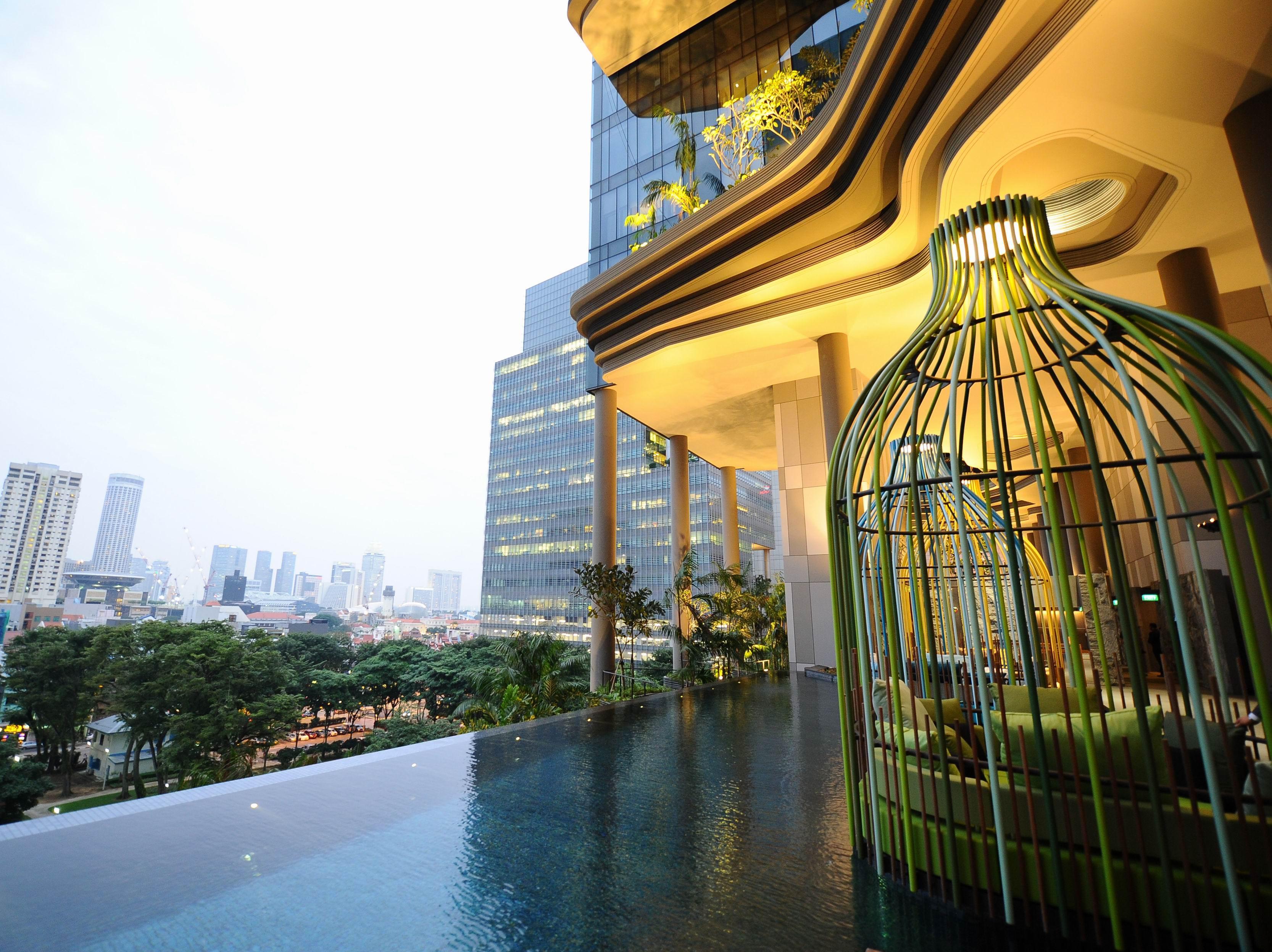 فندق Parkroyal Collection Pickering, سنغافورة المظهر الخارجي الصورة The photo showcases a modern, luxurious space that features an infinity pool with a sleek, reflective surface. In the foreground, there is a unique structure resembling a large birdcage, designed with green elements. The background includes tall city