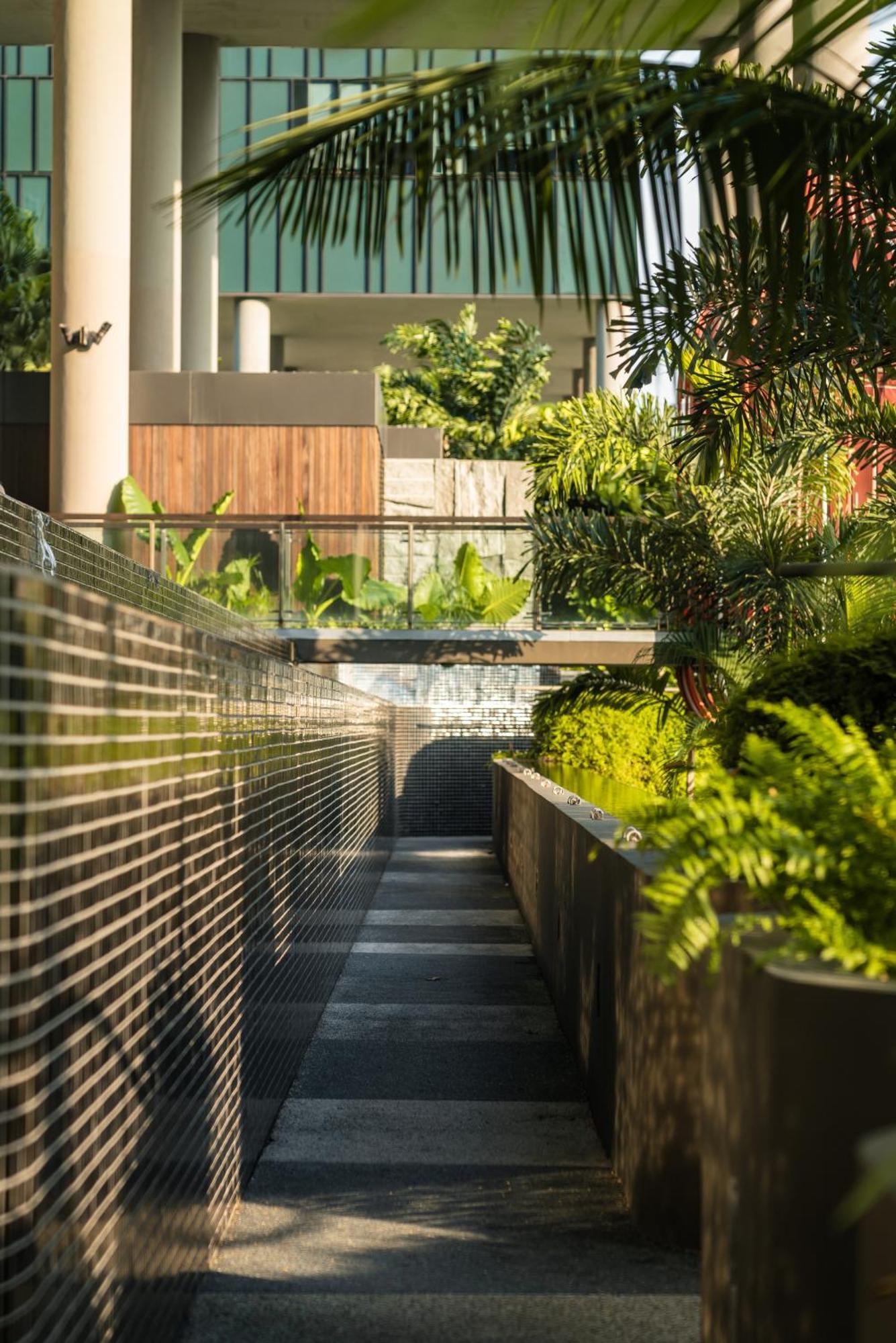 فندق Parkroyal Collection Pickering, سنغافورة المظهر الخارجي الصورة The photo depicts a modern outdoor space featuring sleek design elements. In the foreground, there is a narrow walkway bordered by reflective surfaces. On one side, lush green plants and ferns are arranged in a planter, adding a natural touch to the 