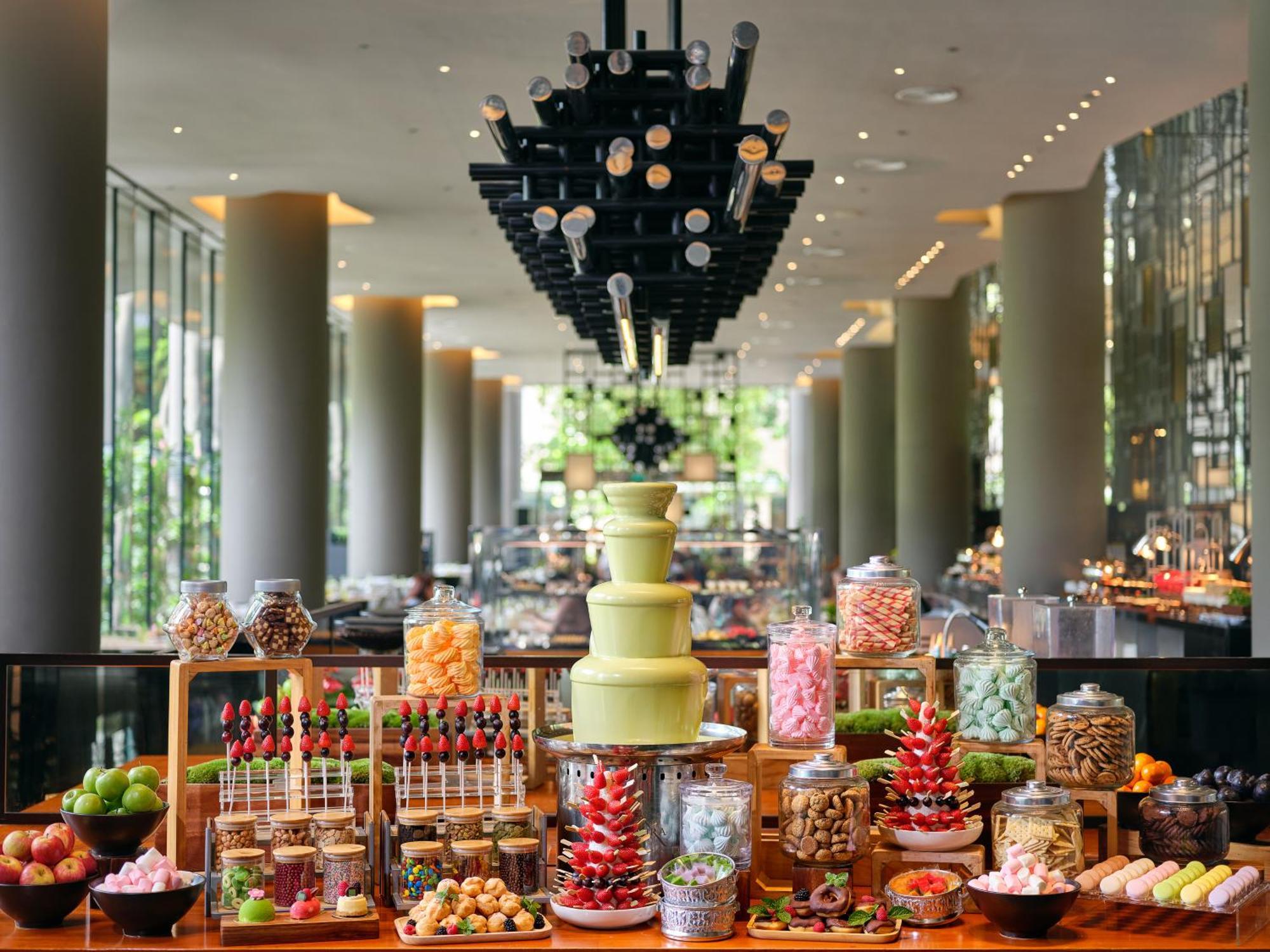 فندق Parkroyal Collection Pickering, سنغافورة المظهر الخارجي الصورة The photo showcases an elegant dessert buffet set up in a modern space. In the foreground, there are various colorful treats displayed, including a tiered cake stand holding an array of sweets. The arrangement features jars filled with candies, choco